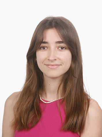 A portrait of a young woman with long brown hair, wearing a pink sleeveless top and a pearl necklace, smiling against a white background.x image sizes